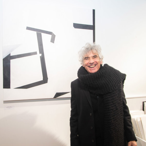 George Levantis standing in front of one of his black and white abstract paintings