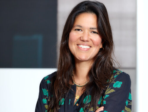 Art specialist and independent art advisor Frances Christie standing with her arms folded, smiling at the camera. She's wearing a navy blue top with turquoise, green flowers.